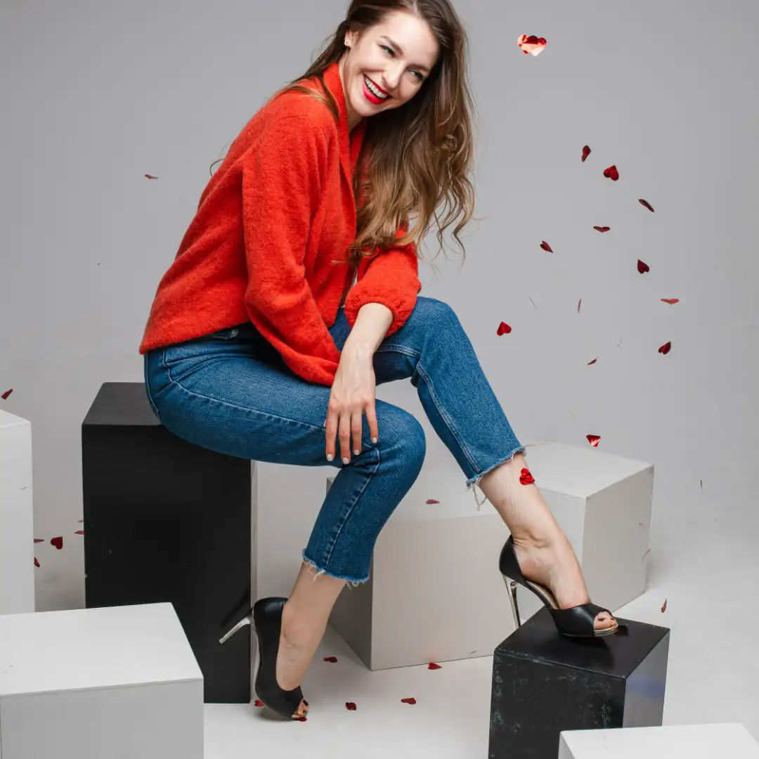 joyful-smiling-young-woman-festive-confetti-wearing-red-sweater-jeans-posing-black-white-cubes-studio-1080